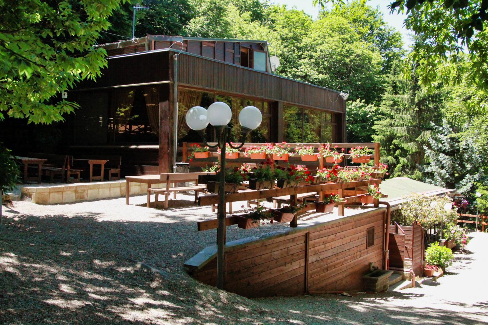 Edificio in legno con terrazza fiorita, circondato da alberi.