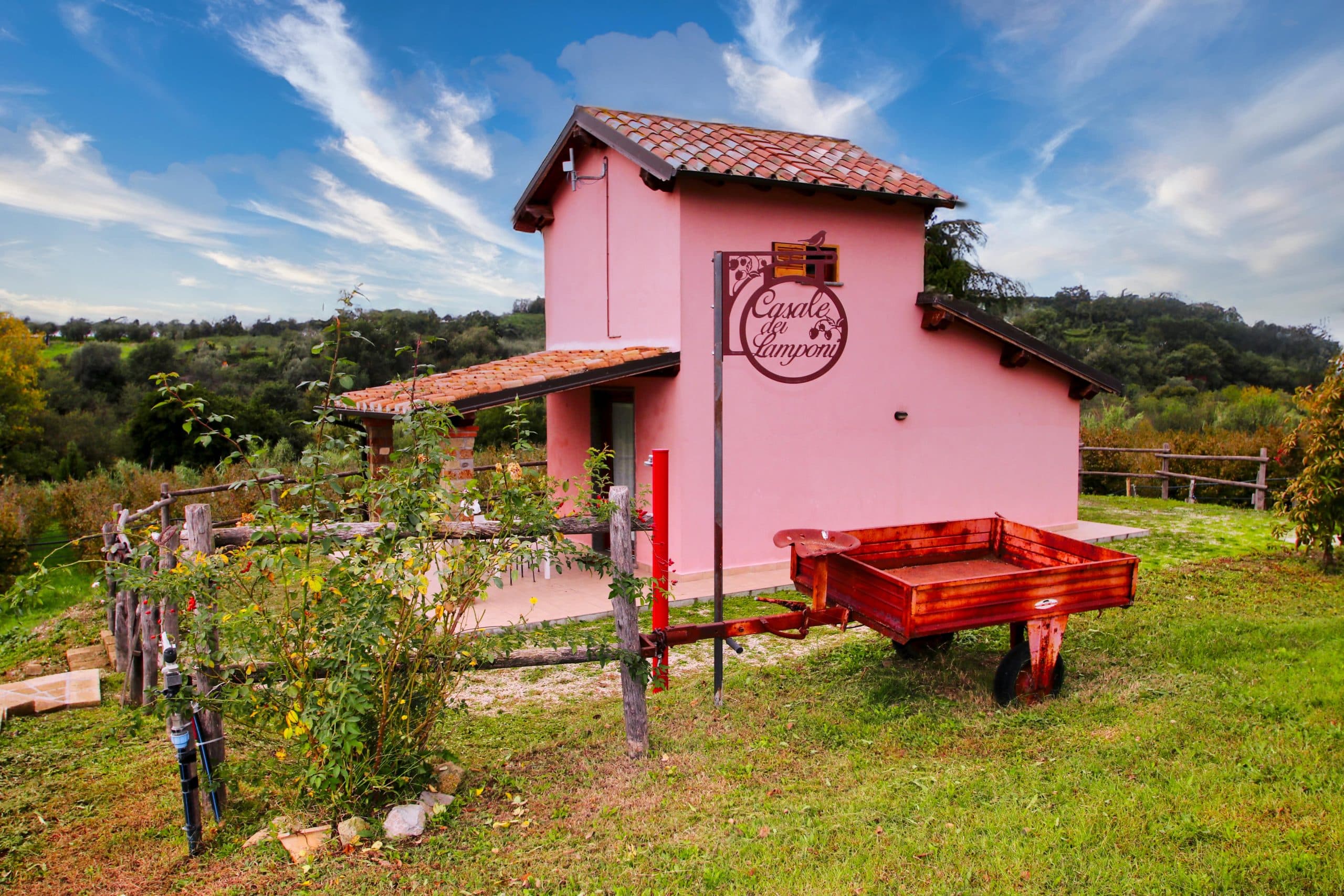 Casa rosa in campagna con carretto rosso sul prato.
