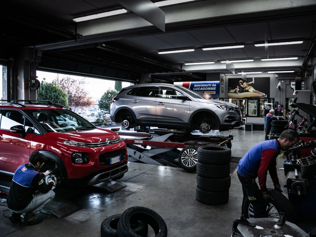 Officina con auto sollevate e meccanici al lavoro.
